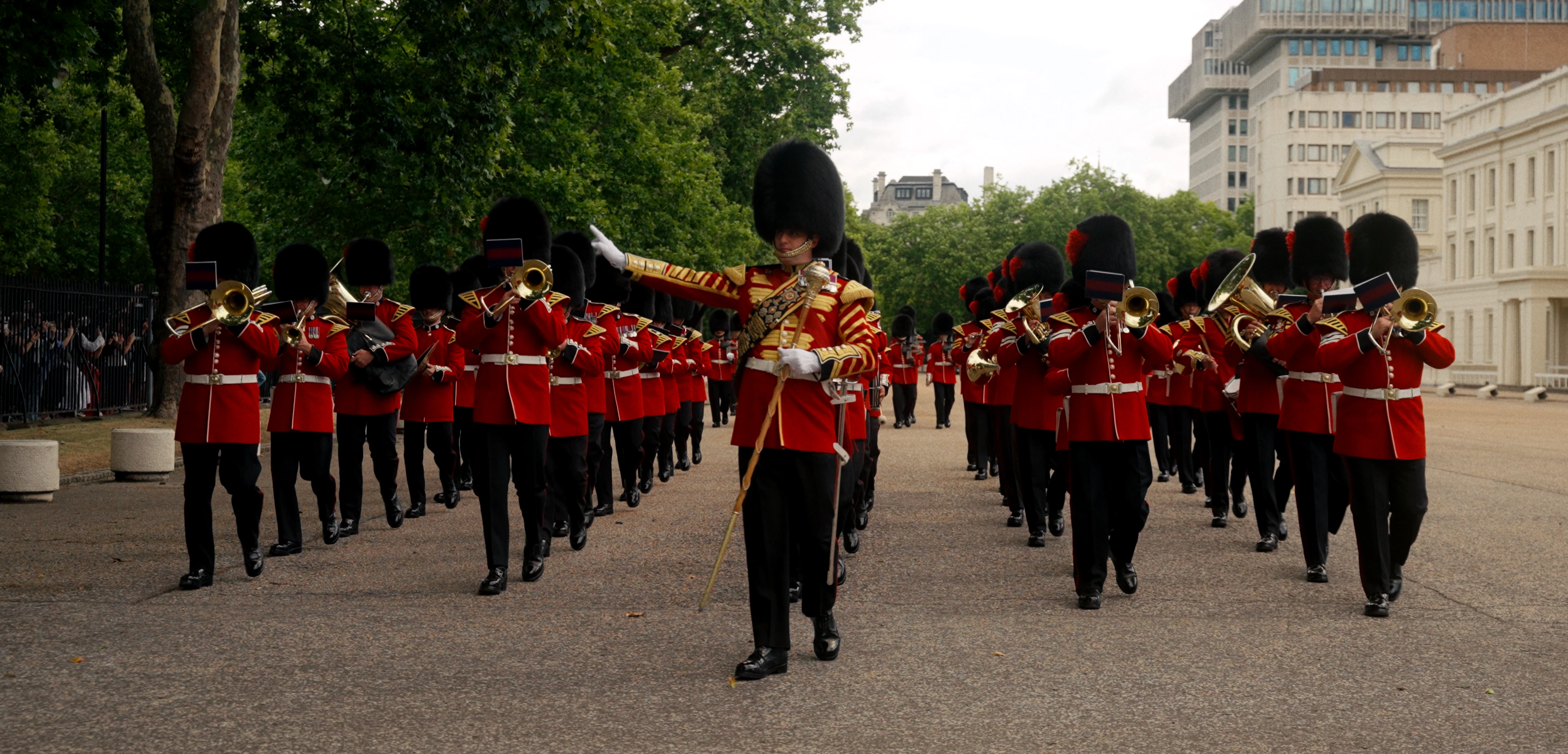 Grenadier Guards marching with instruments inside the military barracks with people looking from outside the fence