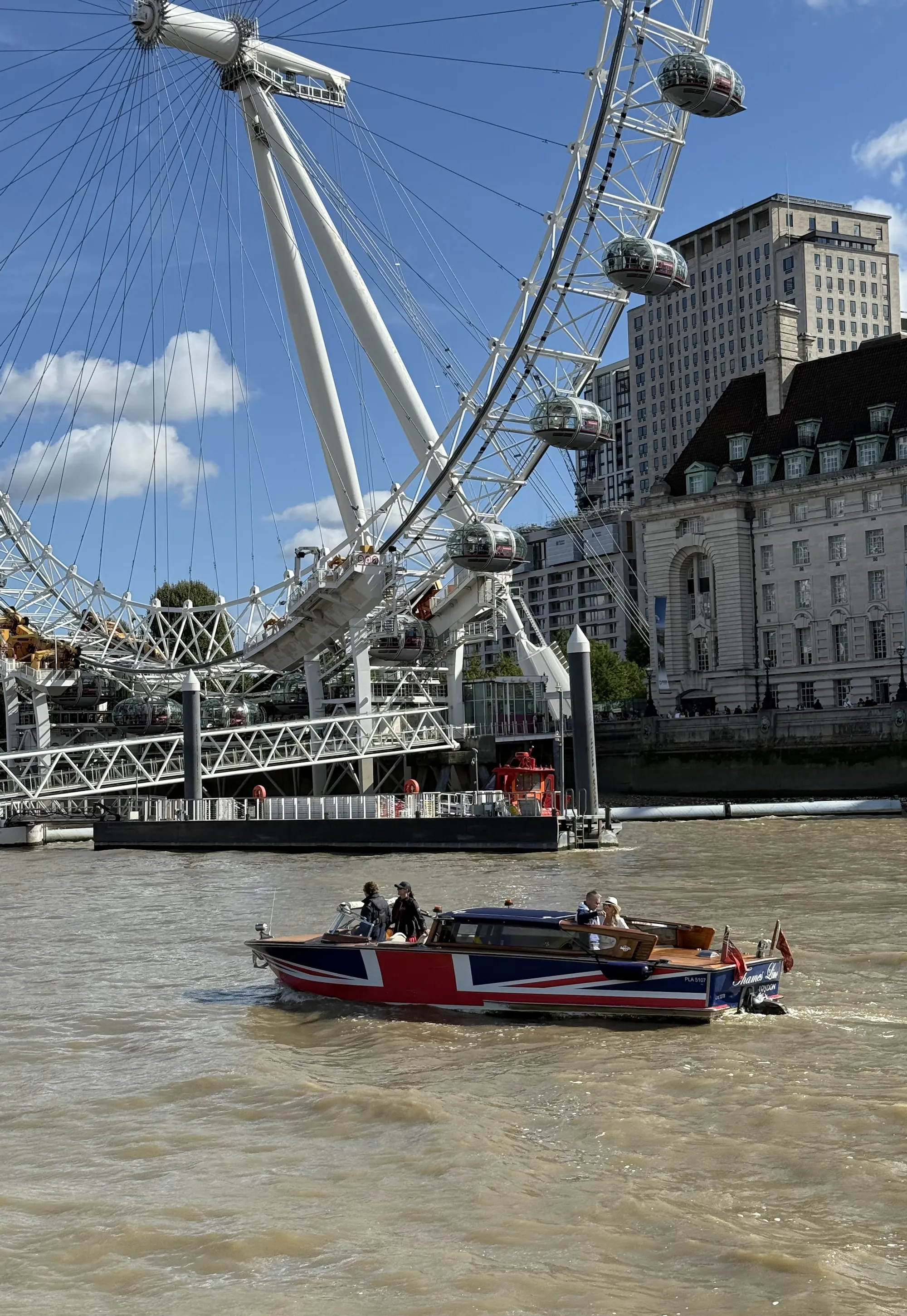River boat decorated with Union Jack sailing on the Thames below the London Eye