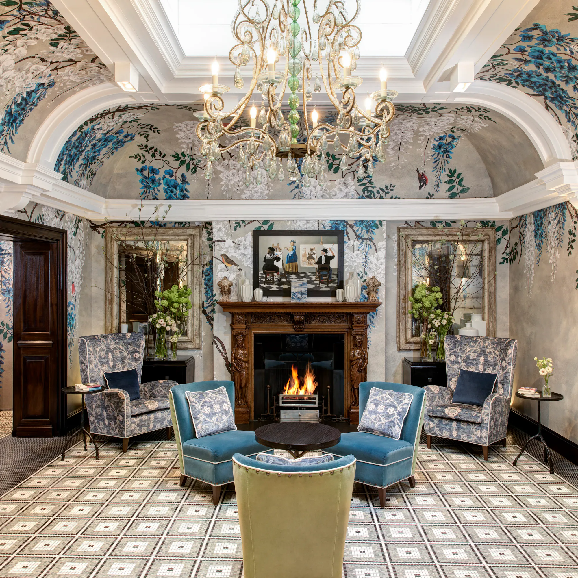 The luxury lobby interior at Brown's Hotel in London with blue upholstered seating, a fireplace, and a crystal chandelier.