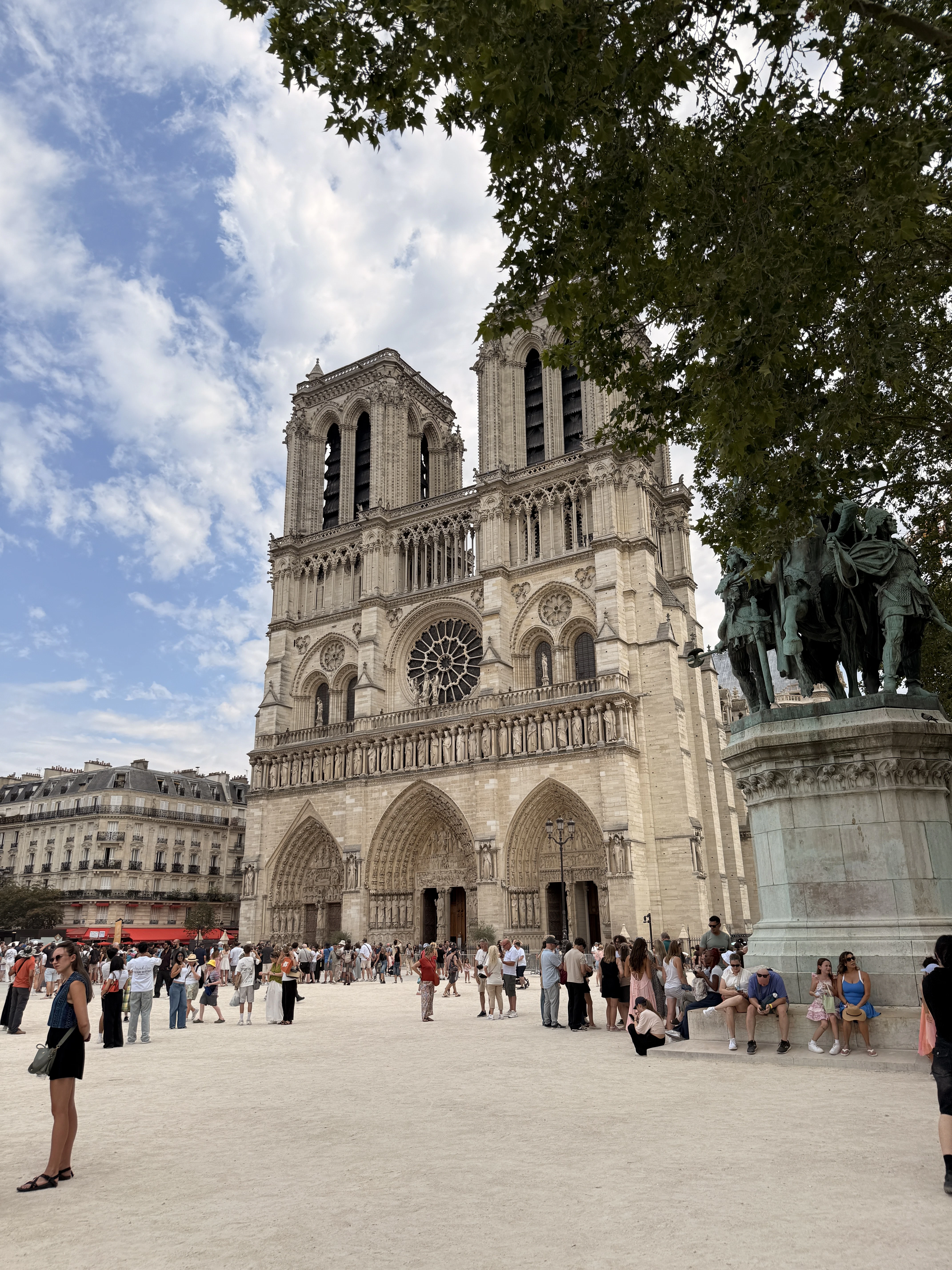 Sunny view of the west facade and twin towers of Notre-Dame in Paris with a small crowd.