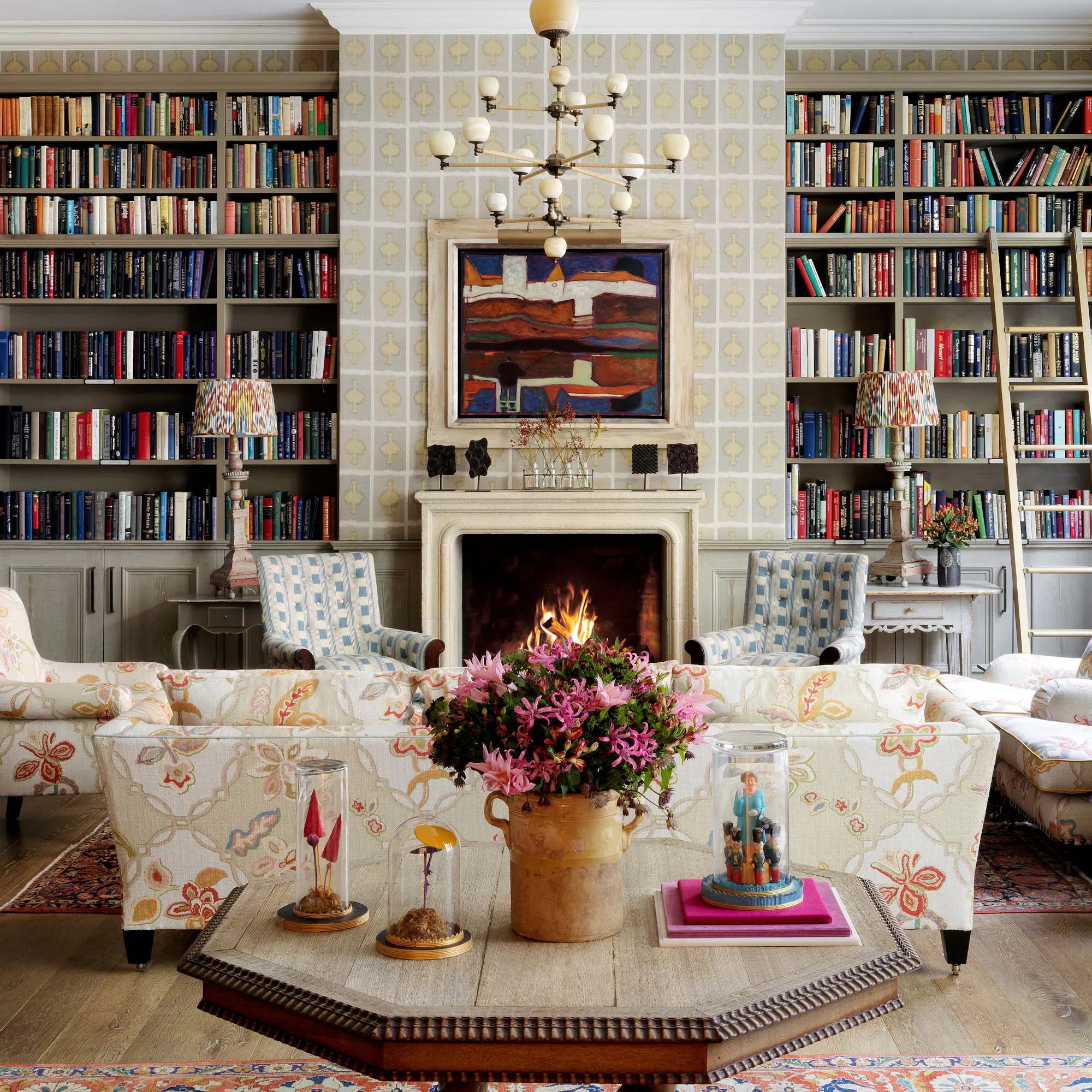 The Library at Ham Yard Hotel, with colourful book-lined shelves and a lit fireplace beside armchairs.