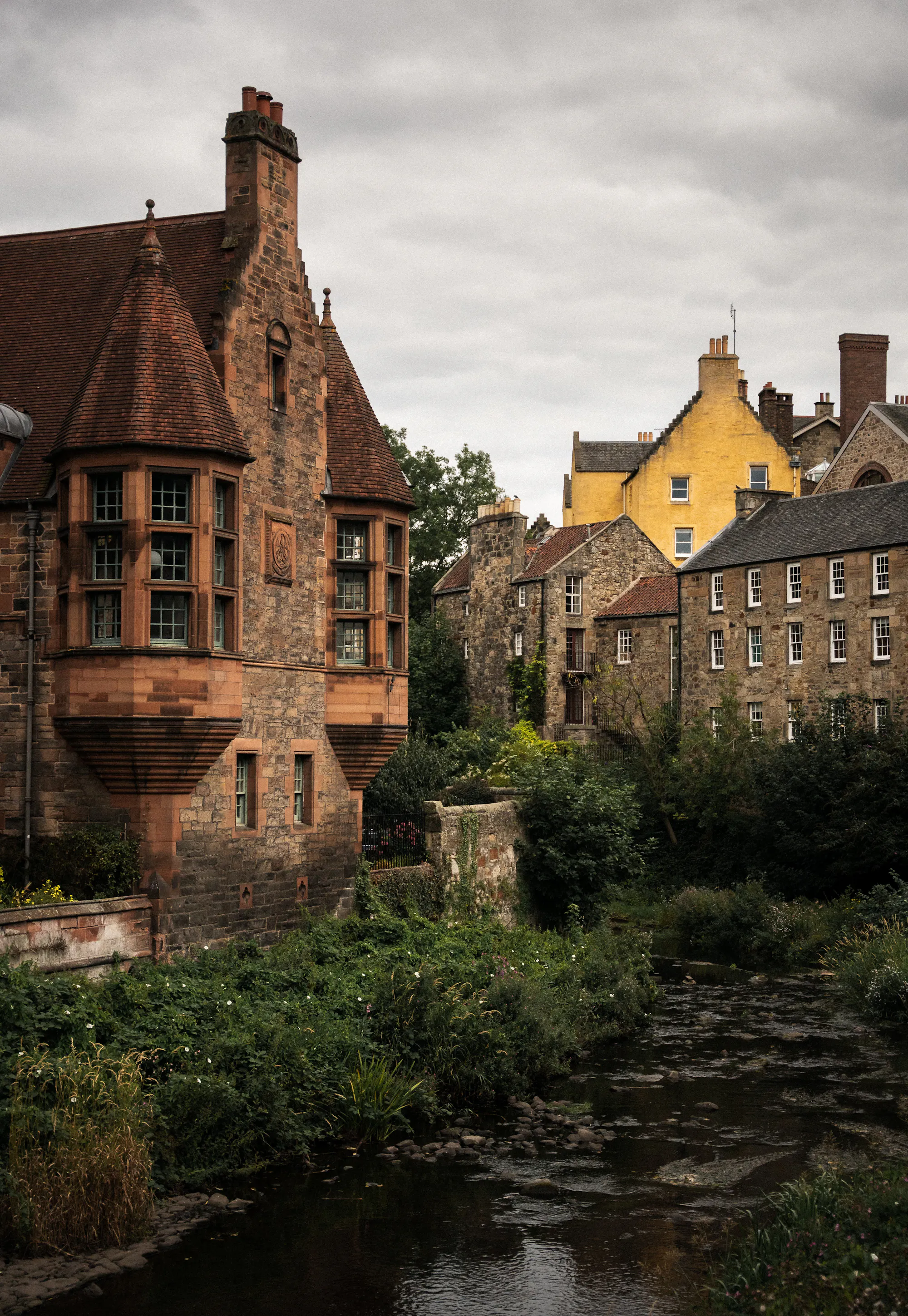 Dean Village's turreted sandstone buildings above the Water of Leith river, a yellow house behind.