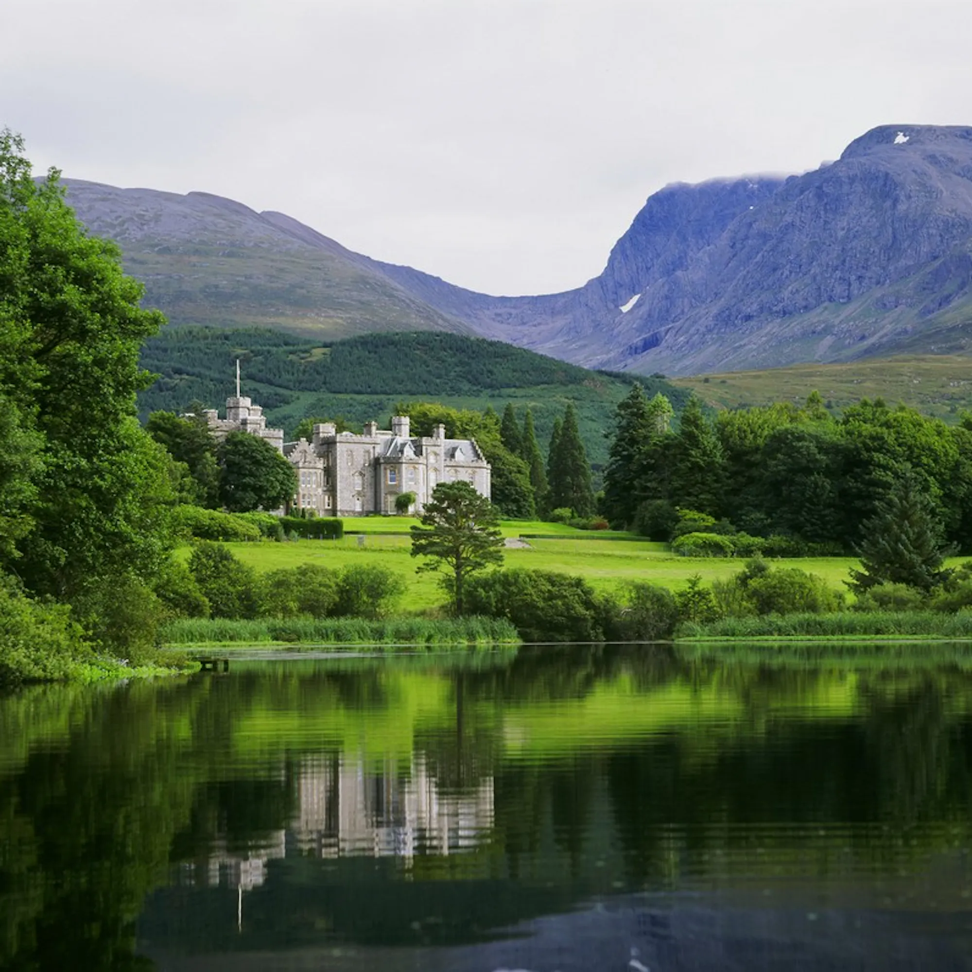 Inverlochy Castle hotel reflected in a loch, with Ben Nevis in the background.
